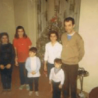 Coloured photo of man, woman and four children in front of Christmas tree.