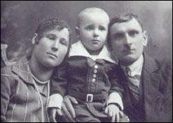 Portrait of mother and father with baby standing between them.