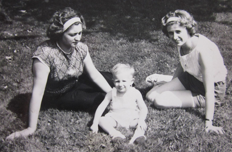 A young boy sits on the grass with two women sitting next to him.