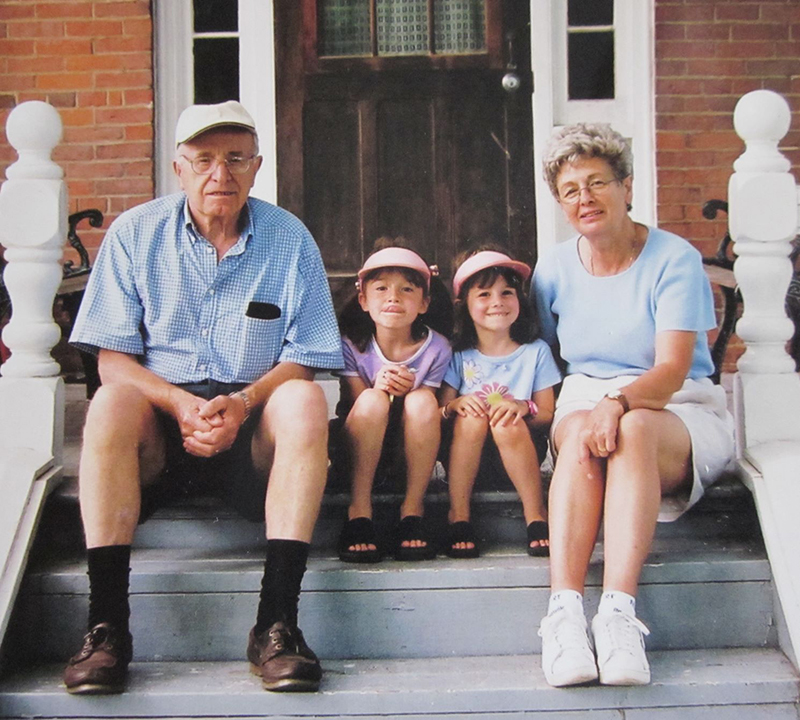 Two small girls sit on the steps of a house with their grandparents next to them.