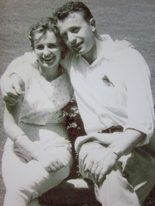 A young man and woman sit on the grass arm in arm.