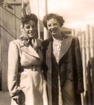 Young Norma standing with woman in white jacket and kerchief.