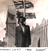 Young Norma, standing in front of buildings with British flags flying in background.