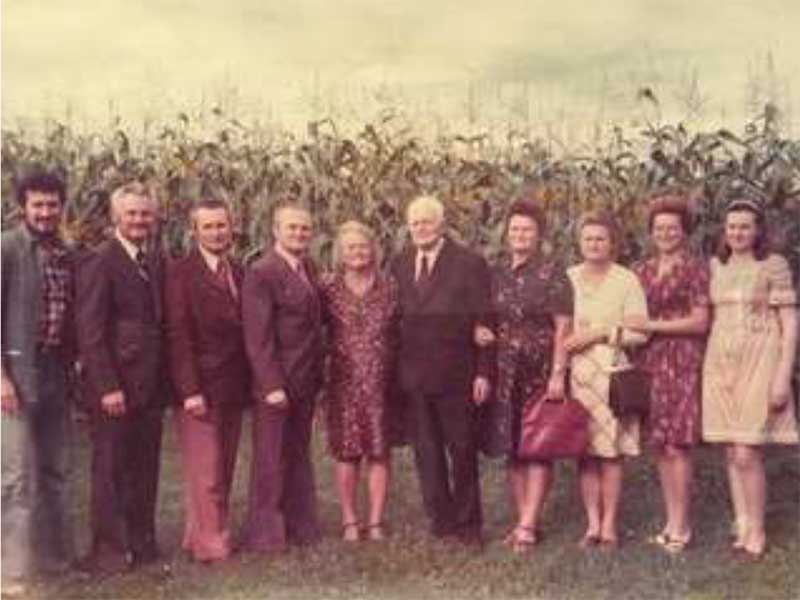 Nine family members standing on grass, with corn field in the background