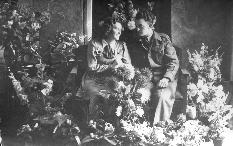 Black and white photo of beautiful couple sitting among flowers.