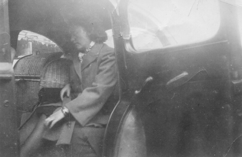 Black and white photo of lady sitting in car with lots of items.