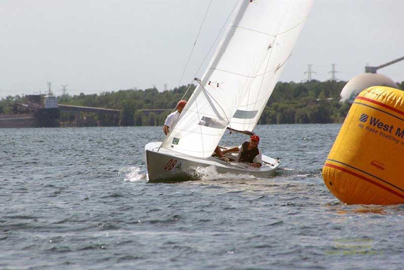 Two men in a racing sailboat veer around a buoy.