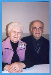 Older Jenny wearing lilac-coloured vest, seated next to Art wearing glasses.
