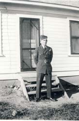 Young Art in uniform, standing in front of building with arms behind back.