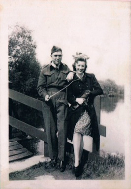 A man and woman sit on the wooden railing of a bridge.