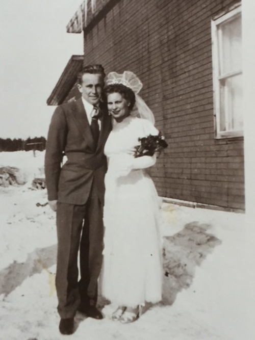 A bride and groom stand in front of a building with arms around each other.