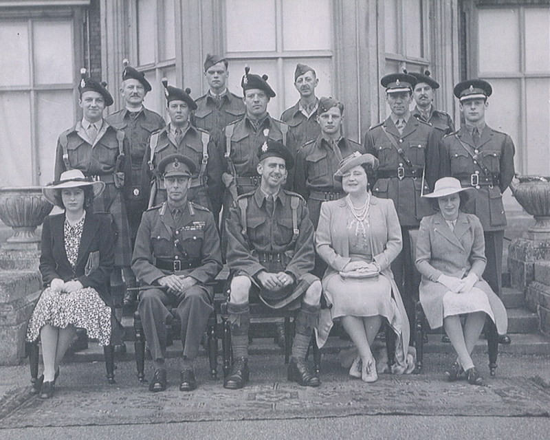 A group of men in military stand behind members of the Royal Family.
