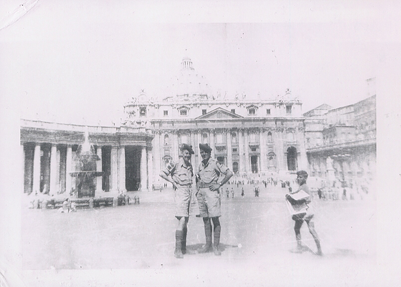 Two men in military uniform stand in a square with a large church behind them.