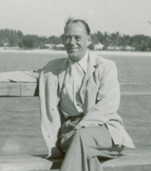 Middle-aged Arthur seated on bench with water in the background.