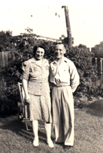 Arthur and wife standing on grass in front of shrubbery.