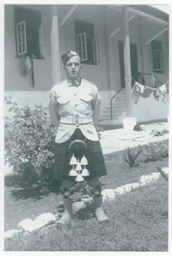 Young Lawrence in a kilt, standing on the grass in front of a building.
