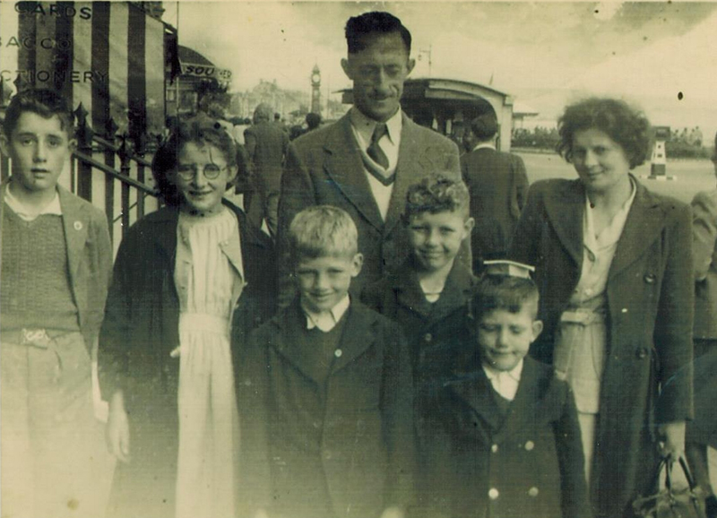 Old black and white image of a couple with their five children standing in front of them.