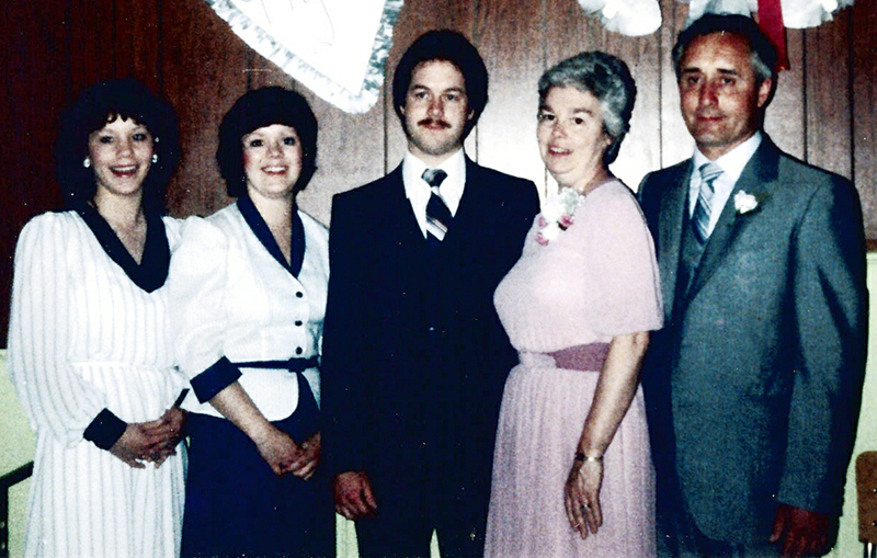 A groom stands on his wedding day, surrounded by his family.