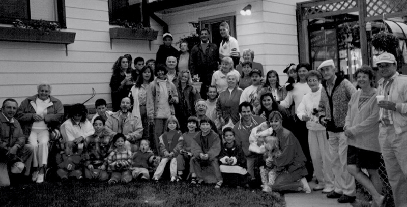 A very large group of men, women and children standing in front of a house and all looking at the camera and smiling.