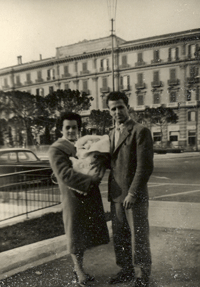 Man and woman with baby, standing in front of big building.