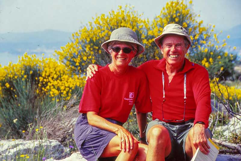 A man and a woman in red t shirts and matching hats sit and smile for the camera.