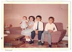 Small colour photograph of a mother sitting on a pink couch with three children. 