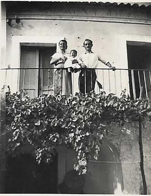 Man, woman and baby lean against a railing and look down from their balcony.