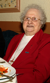 Sister Liota in a red jacket, sitting at the table.