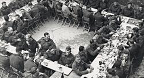 Group of uniform men sitting on the food tables.
