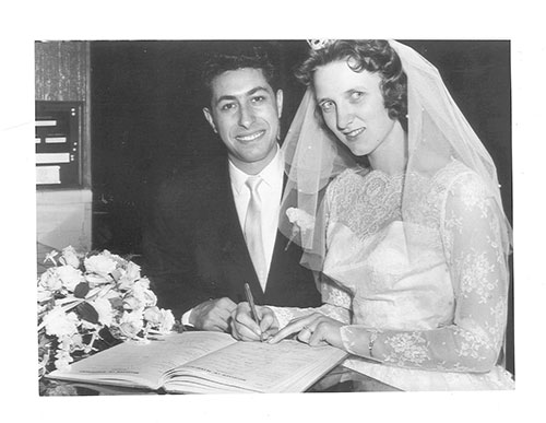 A bride and groom sit at a desk and sign a wedding book.