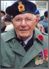 Recent photo of older Elmo, wearing beret, medals and poppy on jacket collar.