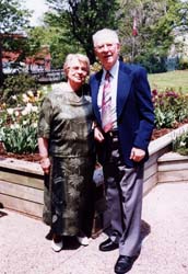 Recent photo of Marianne and Lawrence with gardens behind them.