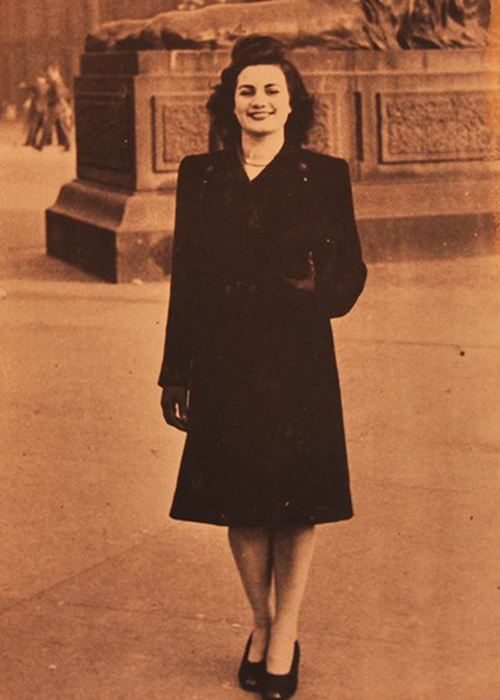 Sepia photo of young woman in a black coat standing in front of a statue.