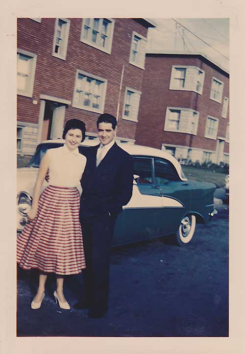 Man and woman stand in front of an old car.