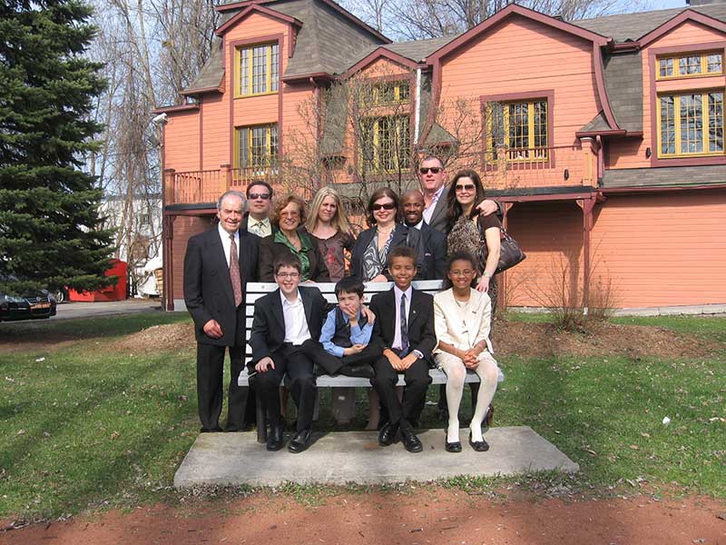 Four children sit on a bench with eight adults standing behind them.