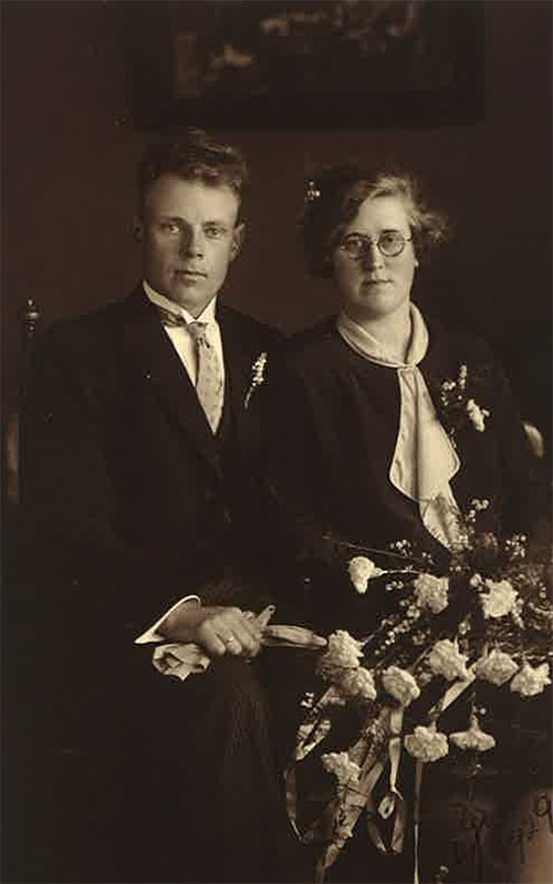 Man and woman wearing black clothes sitting on chair, the woman has flowers in her lap.