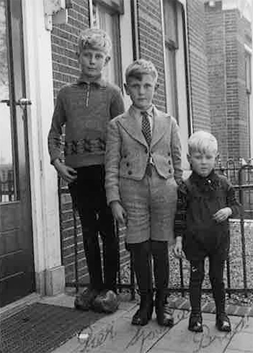 Three kids are standing in front of a fence to have their photo taken.