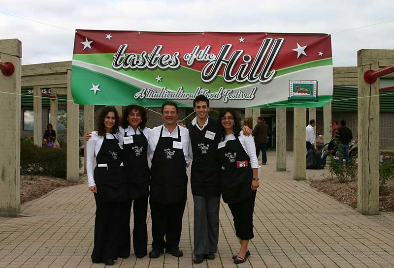 Five family members in aprons stand in front of a sign reading Tastes of the Hill.