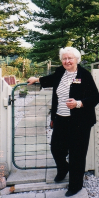 Catherine older, dressed in black and standing against a barrier.