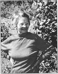 Irene as an older woman, standing in front of shrubbery.