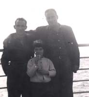 Two men and one small boy leaning against railing of ship.
