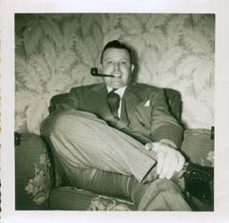 Young Gerald sits on the couch, smoking a pipe.