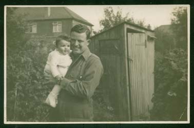 Sandra as a baby in her father's arms, with wooden shack in background.
