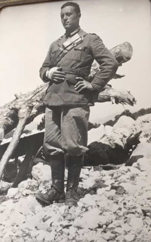 Archival photo of a soldier standing with one hand on his hip and the other wrapped in bandages.