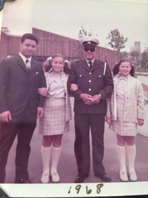 A man in uniform is standing with another man and two young girls.