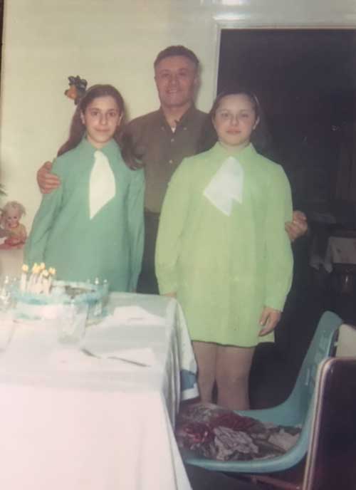 Two girls in lime green dresses stand on either side of their father.