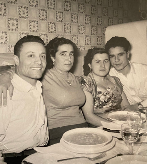 Two couples seated at a dinner table pose for the camera.