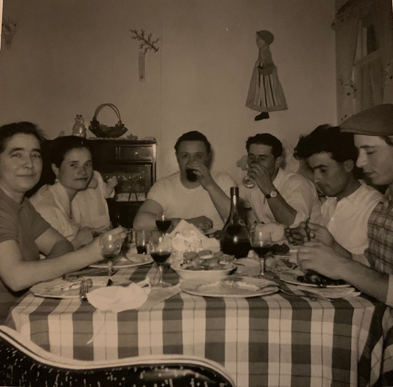 Small group of men and women seated at a table, eating and drinking.