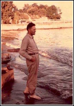 A young man is standing on the edge of the water, he is barefoot.
