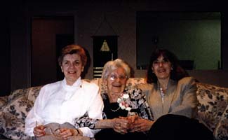 Recent color photograph of three women sitting on the couch of a living room.